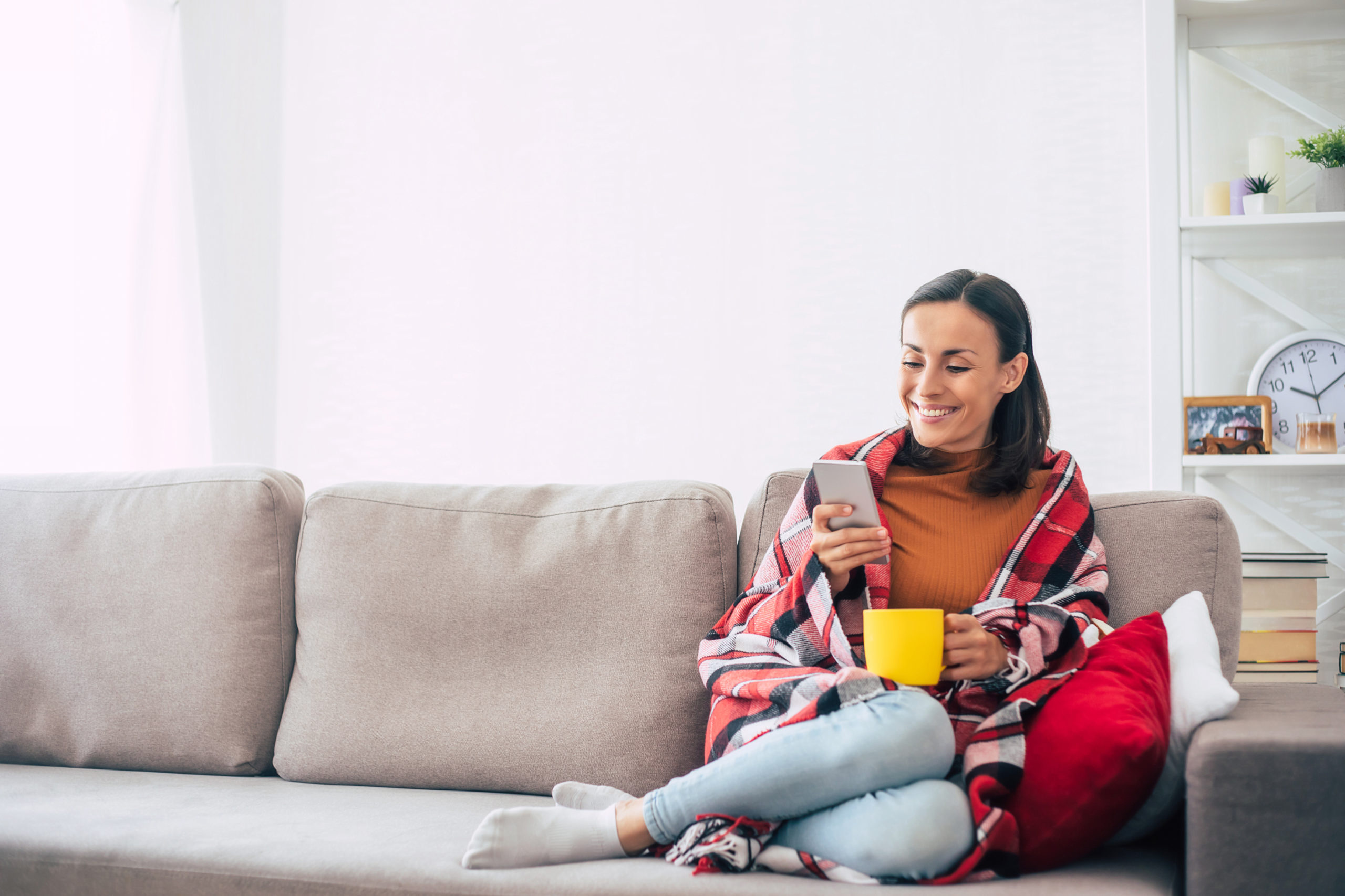 Happy woman sitting on the sofa and smiling while using her smartphone.