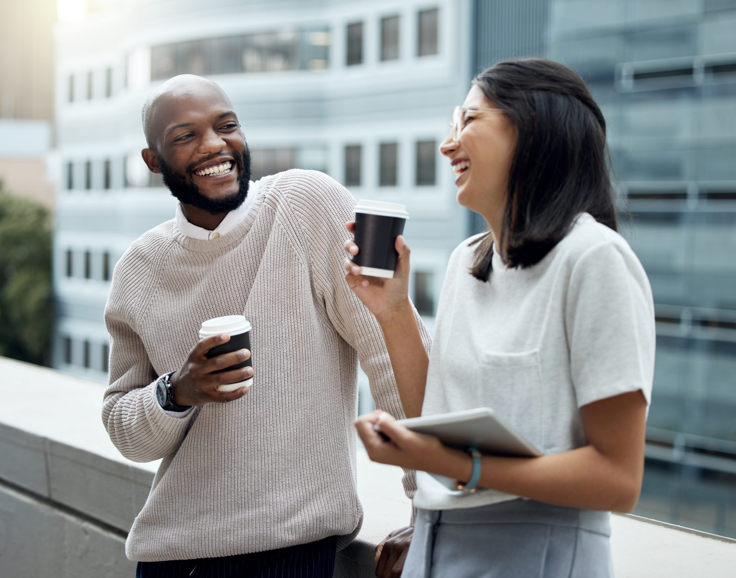 Man and woman standing on a balcony holding cups of coffee and smiling at each other after meeting on a doctor dating site.