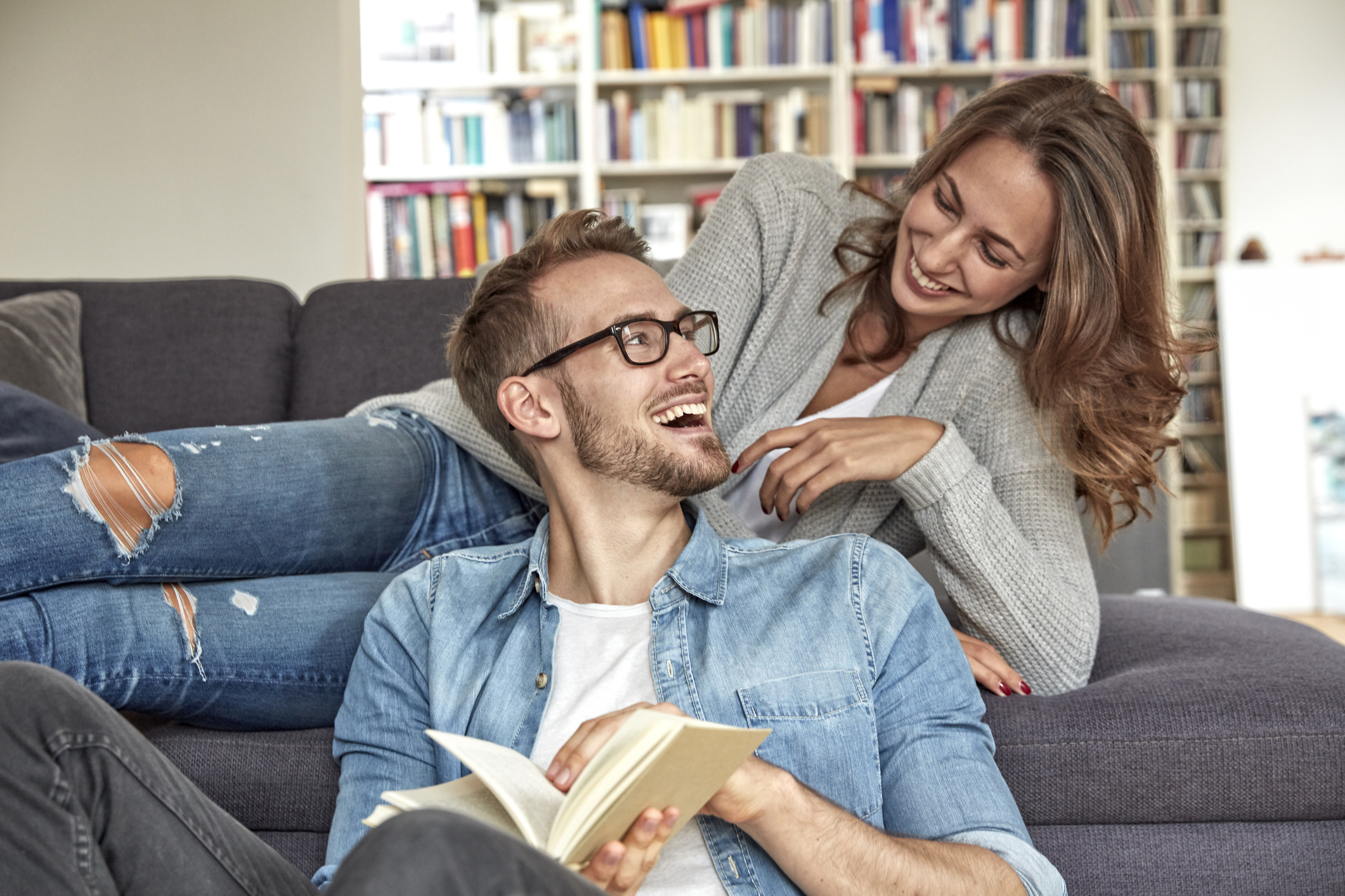 Happy couple relaxing and laughing together on the sofa while reading one of the best relationship books.