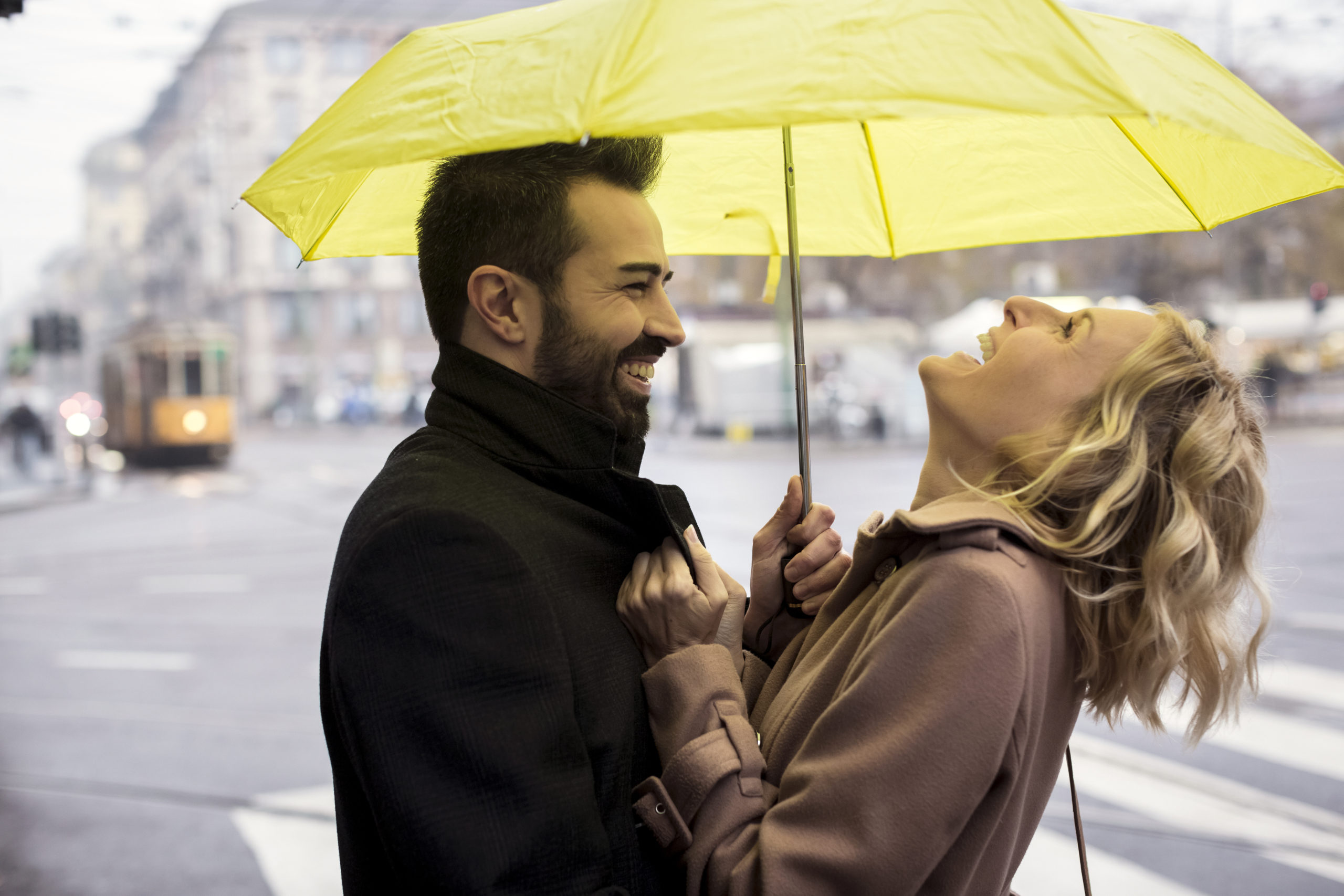 Happy man and woman standing under umbrella in the city and laughing.