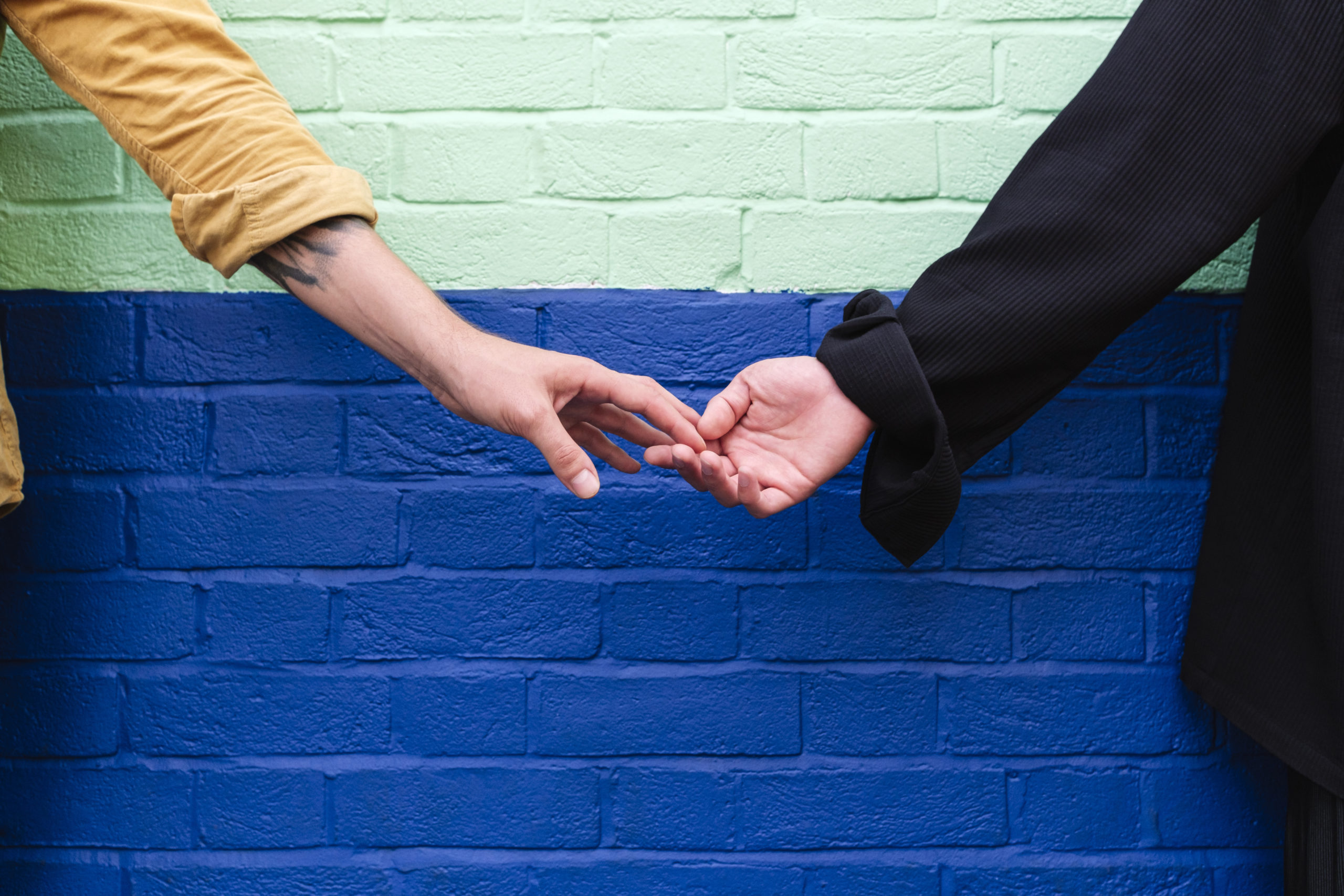 Couple holding hands in front of colorful wall after meeting in one of the best cities for dating in your 40s.