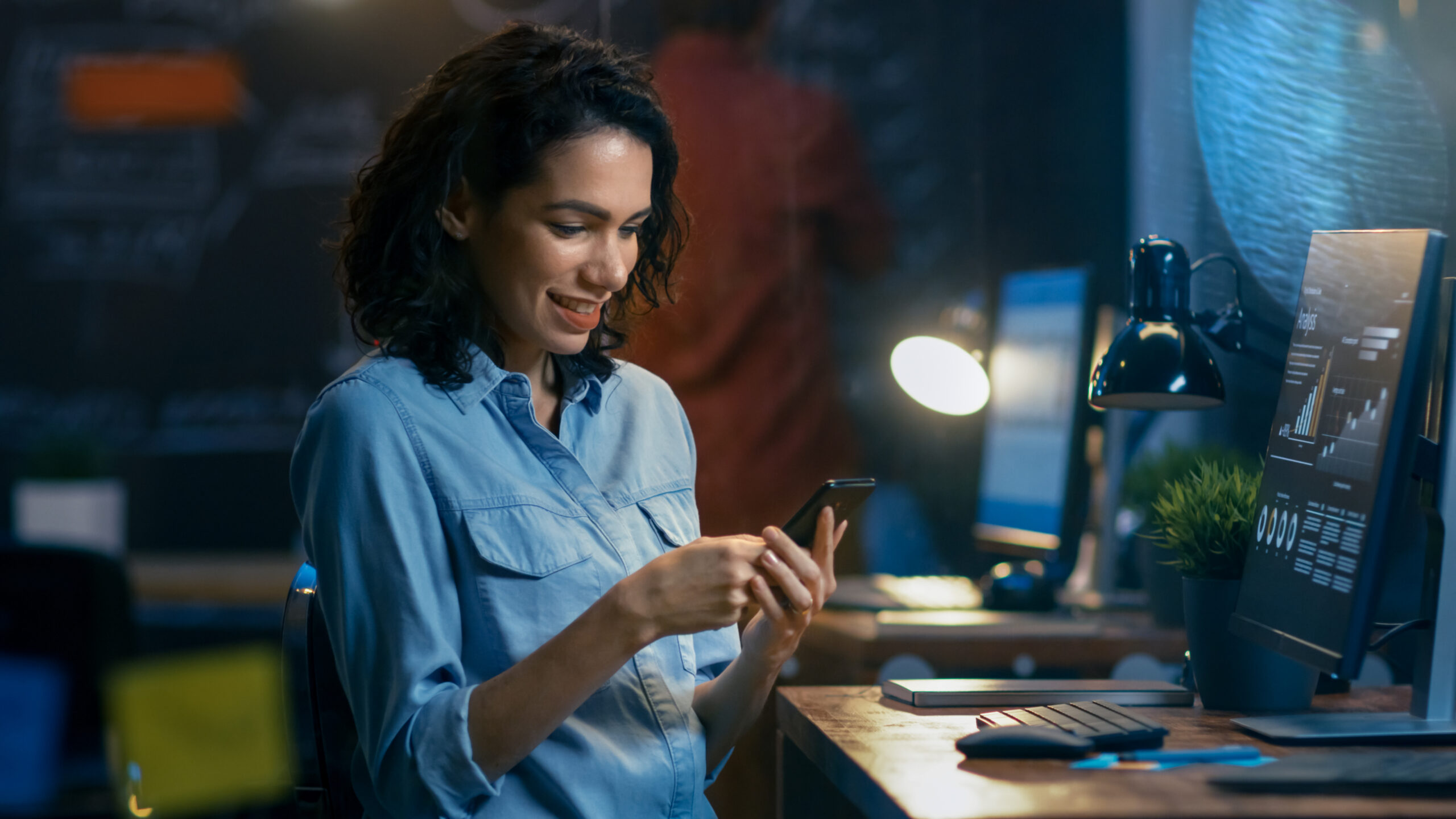 Woman at her work station looking at a smartphone.