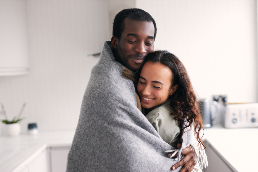 Couple embracing under a blanket while standing.