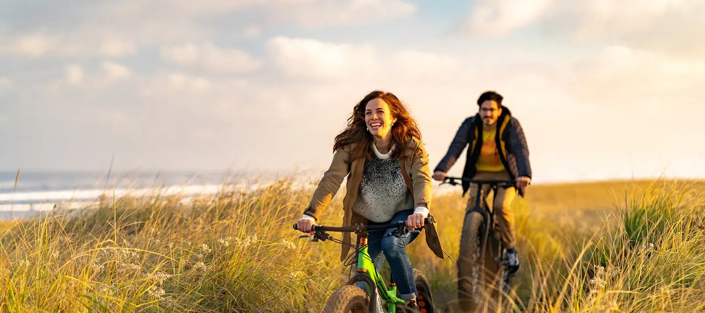 Two people ride bicycles along a scenic path by the ocean